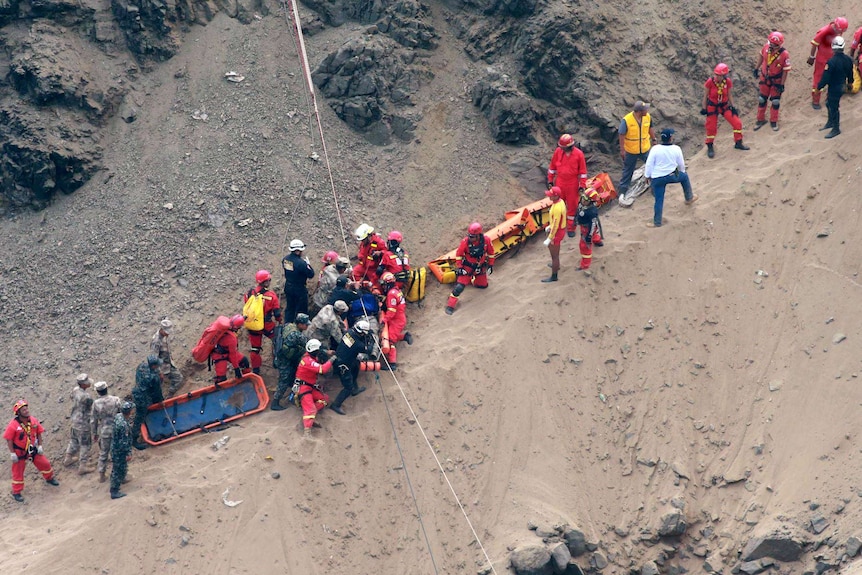 Rescue workers haul stretchers up a narrow, sandy slope.
