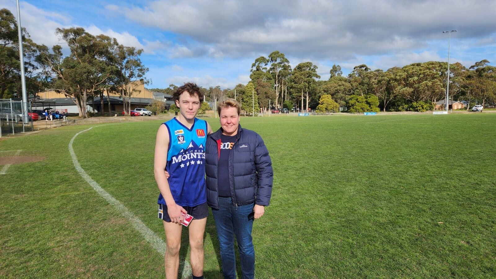 A teenage boy, wearing footy gear, and woman on a footy oval.