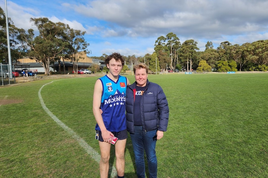 A teenage boy, wearing footy gear, and woman on a footy oval.