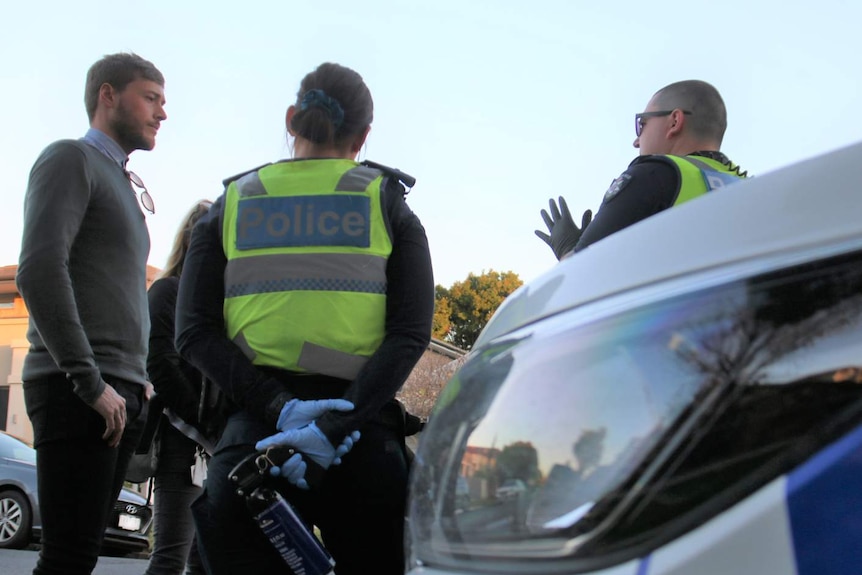 A male and a female police officer stand on a suburban street speaking to another man and woman.