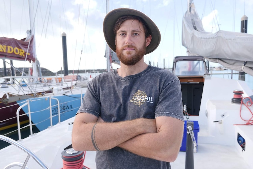 Josh Wilde stands with his arms folded on a boat at a marina in Airlie Beach.
