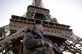 A French soldier, holding a high-powered gun, stands guard under the Eiffel Tower.