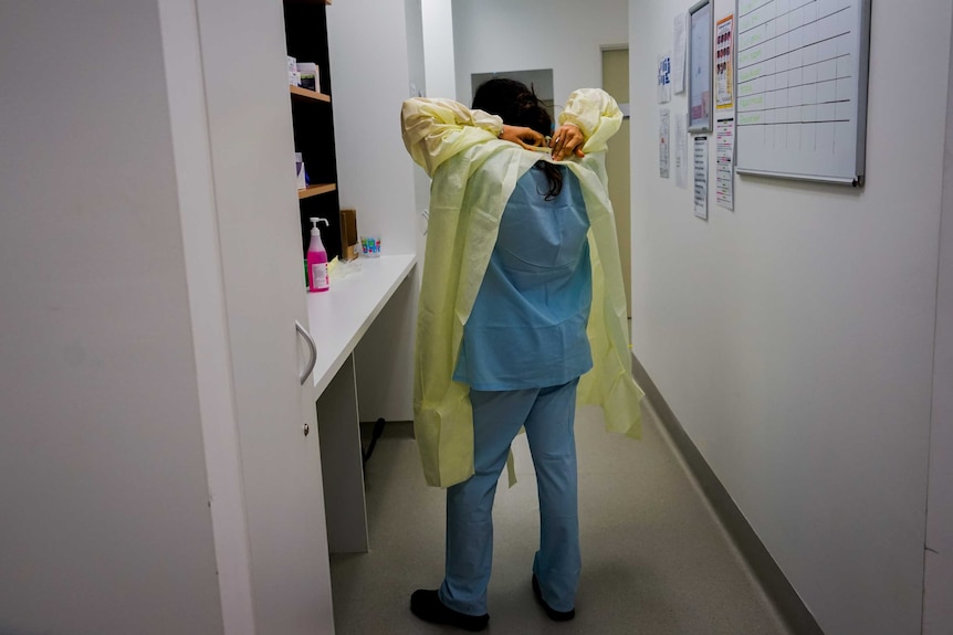 The back of a health worker who is putting on a full protective uniform.