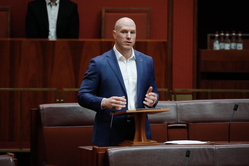 Man wearing blue suit speaking at a podium in the Australian Senate. 