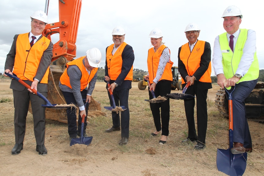 Six people in hi-vis vests holding shovels and looking at the camera.