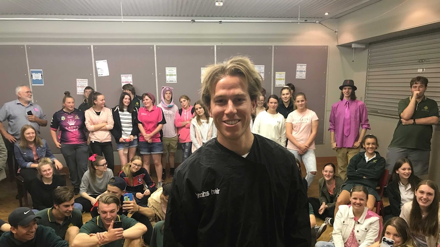 Teacher Josh Vater in front a room of students at teachers after having his hair cut to donate to be made into a wig.