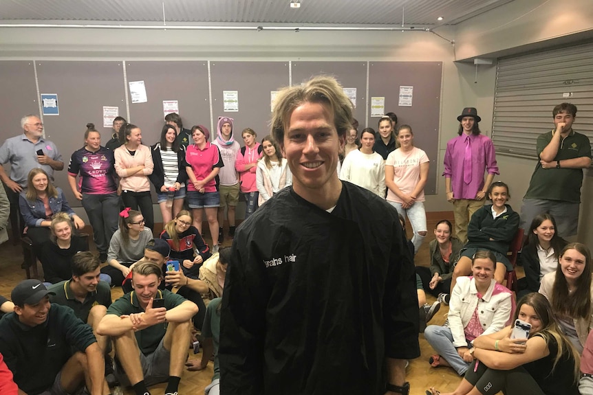 Teacher Josh Vater in front a room of students at teachers after having his hair cut to donate to be made into a wig.