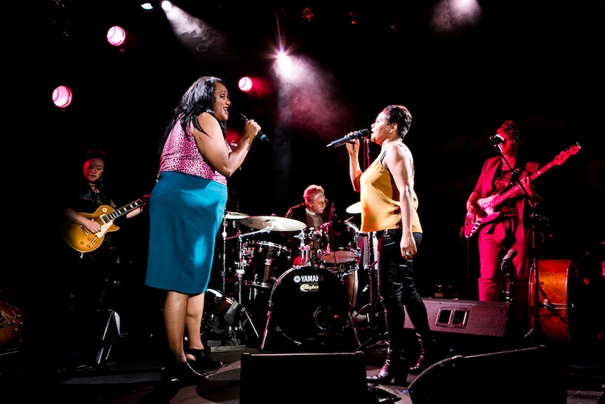 Colour production still of Elaine Crombie (left) and Ursula Yovich (right) singing on stage.