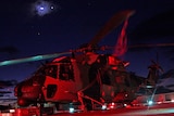 A picture of a helicopter awash in red light with a partly-obscured moon above.