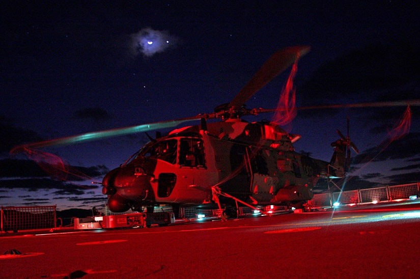 A picture of a helicopter awash in red light with a partly-obscured moon above.