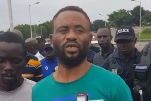 A man with a beard surrounded by other men in Congo, Africa, speaking into a recorder