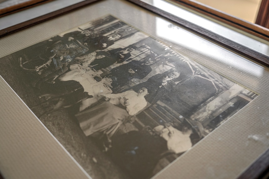 A black and white photo in a frame with a group of men and women drinking tea.