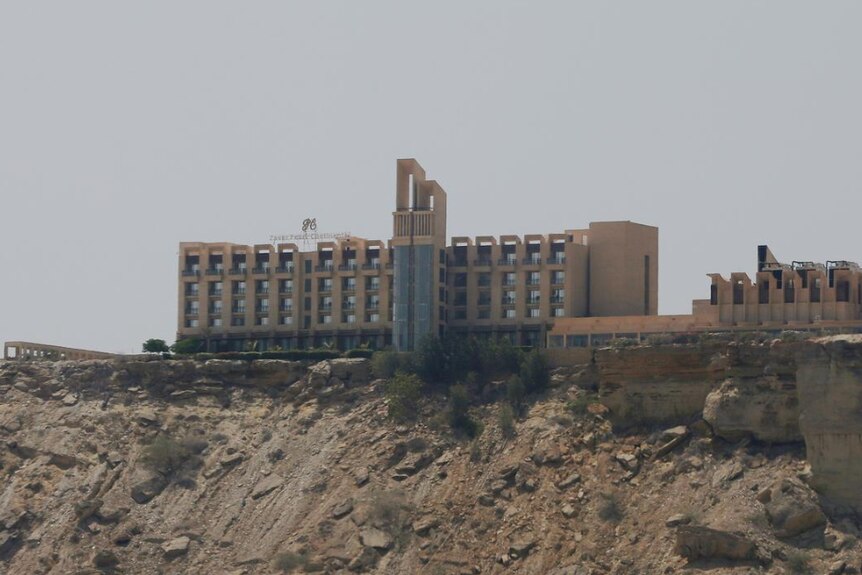 A beige hotel sits on top of a rocky ridge