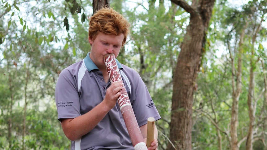 Indigenous teenager Michael James playing the didgeridoo in a native forest.