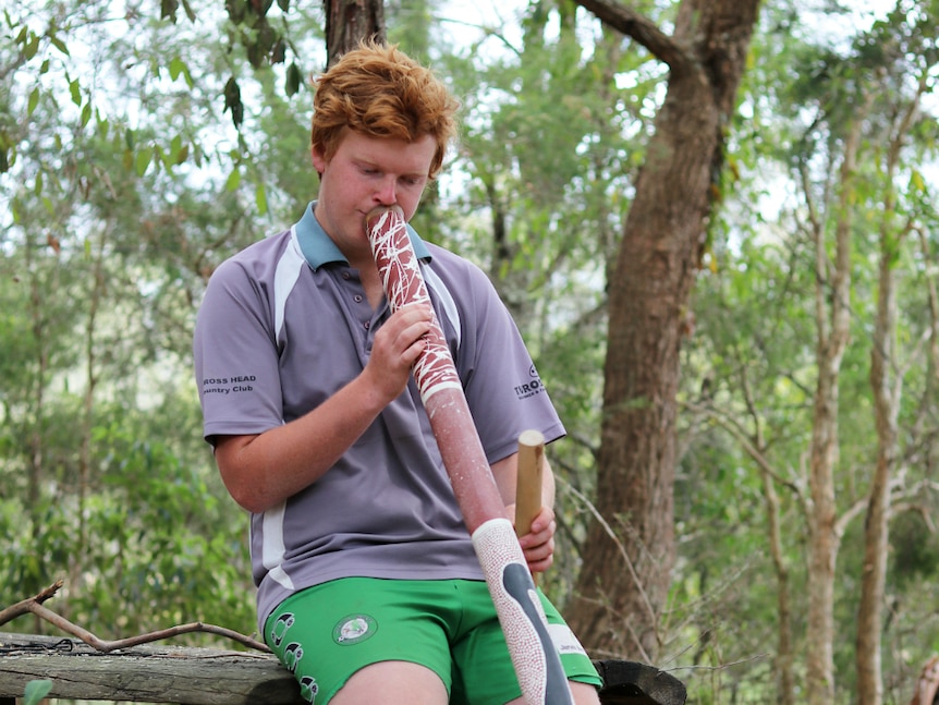 Indigenous teenager Michael James playing the didgeridoo in a native forest.