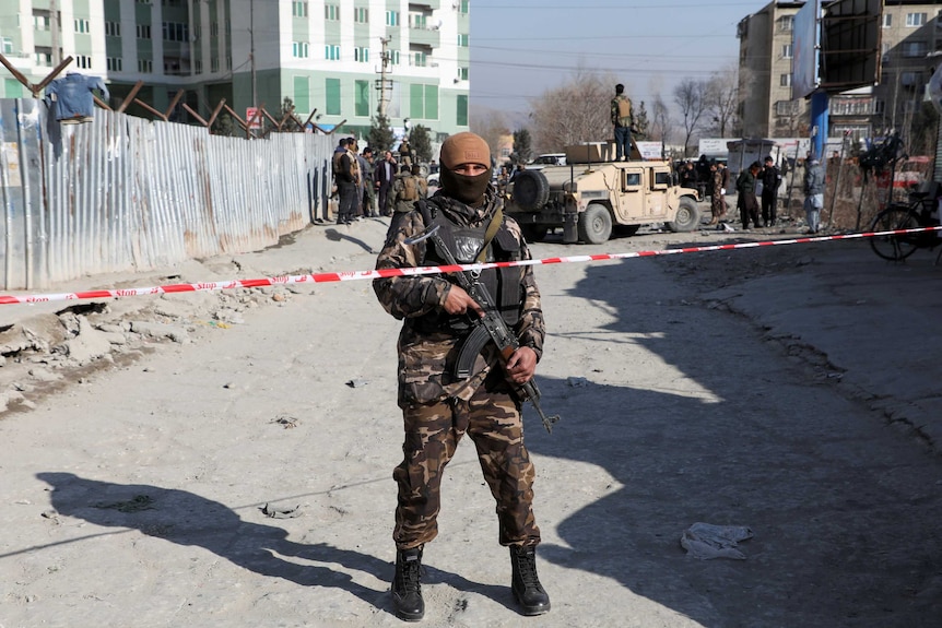 An Afghan security officer stands in front of tape at the site of a bomb blast.