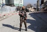 An Afghan security officer stands in front of tape at the site of a bomb blast.