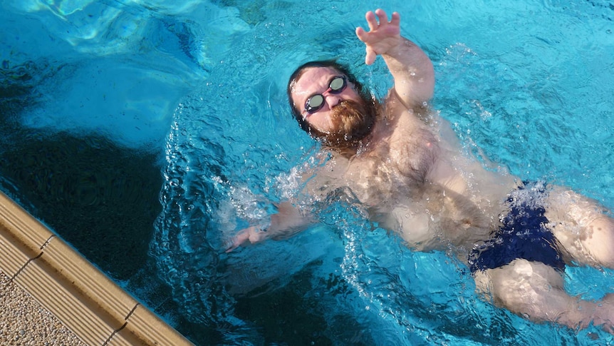 Man with goggles does backstroke in a swimming pool.