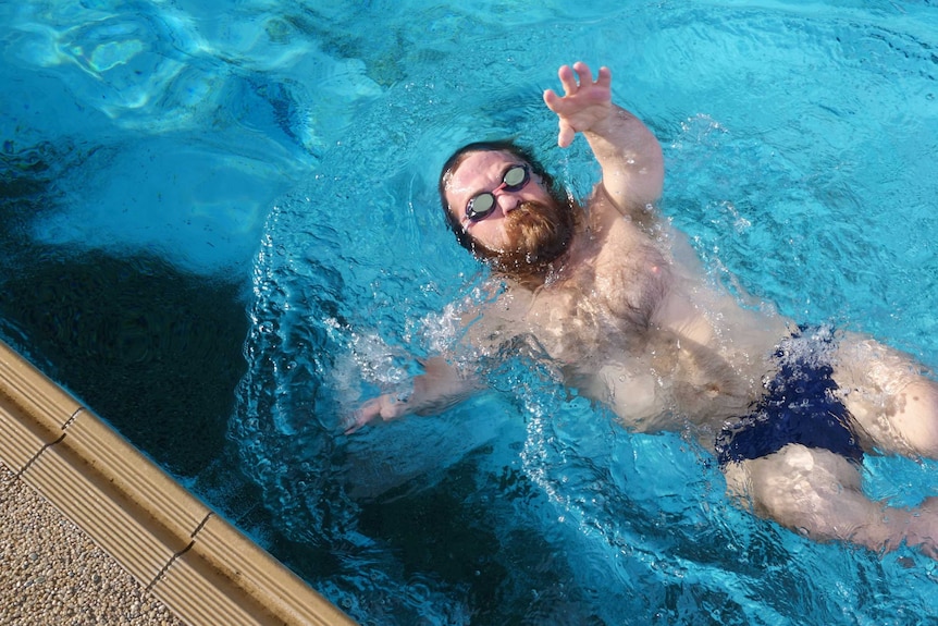 Man with goggles does backstroke in a swimming pool.