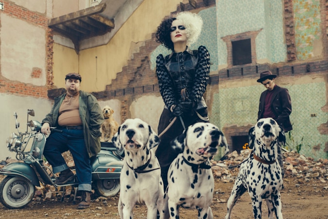 Film still of Paul Walter Hauser leaning on a motorbike and Joel Fry, while Emma Stone holds three dalmatians on a leash