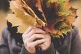 A woman hiding her face behind a big handful of autumn leaves.