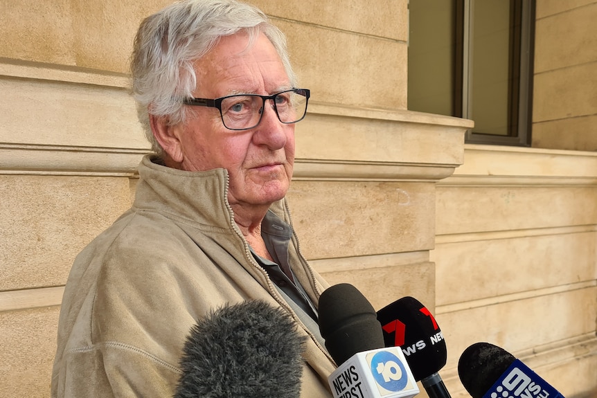 A man in a khaki jacket and glasses speaking to microphones outside court