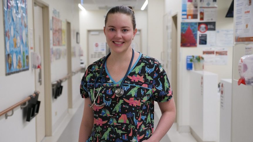 Dr Erica West, a paediatric doctor in Mount Isa, stands in a hospital hallway in her scrubs, which are covered in dinosaurs.