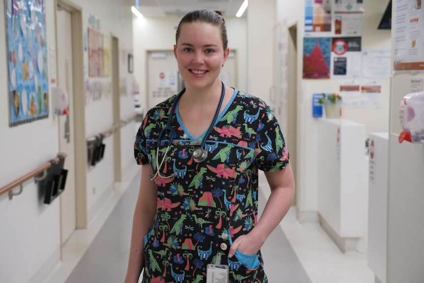 Dr Erica West, a paediatric doctor in Mount Isa, stands in a hospital hallway in her scrubs, which are covered in dinosaurs.