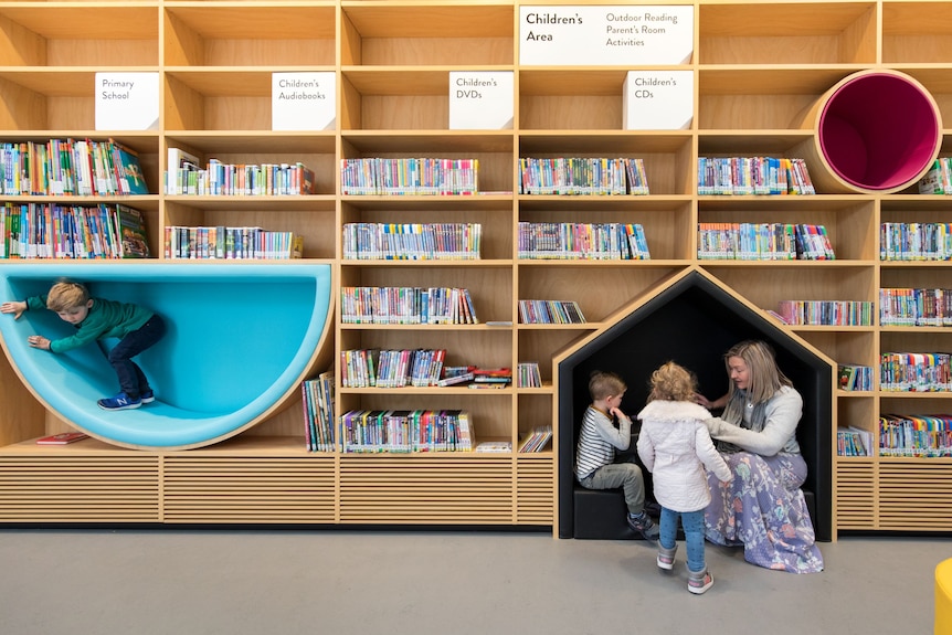 A mother and her children read books and play in a library.