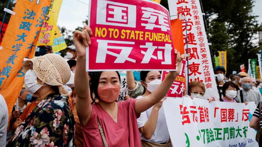 Woman holds sign says 'no to state funeral' among protesters