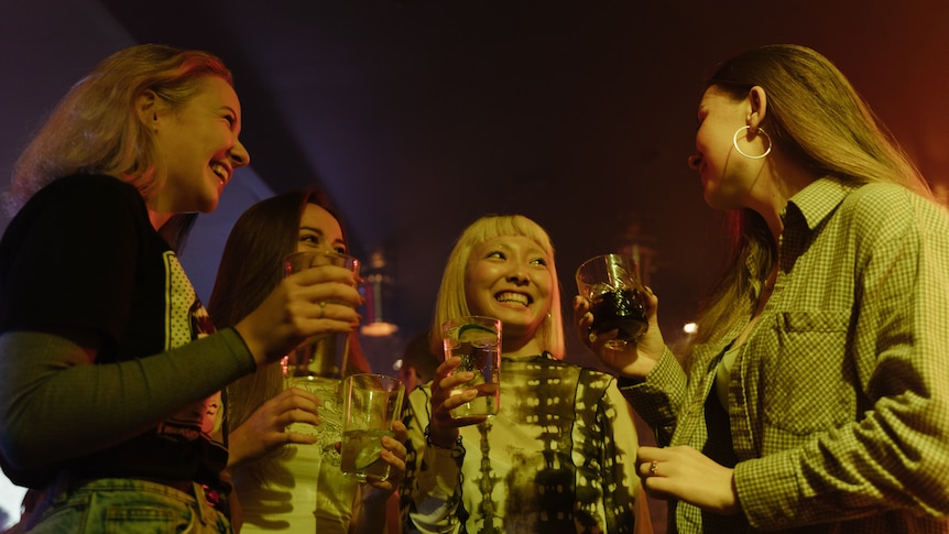 Four women smile at each other while holding drinks. 