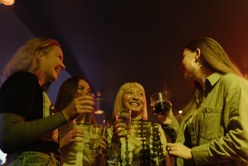 Four women smile at each other while holding drinks. 