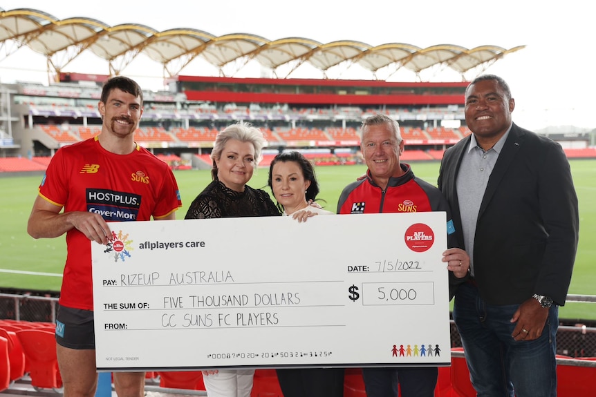 Gold Coast Sun's vice-captain Sam Collins hands over a check from the players for RizeUp.