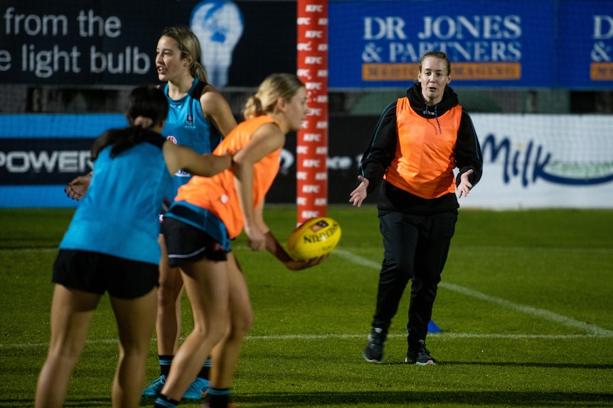 Four women in blue and orange vests playing footy on the field.