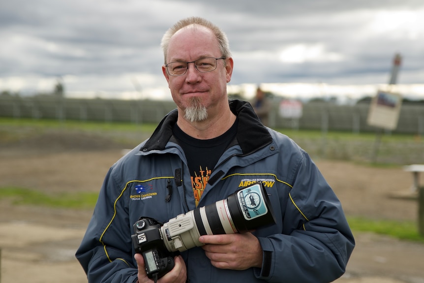 a man with a beard and glasses who is smiling.  he is holding a camera.