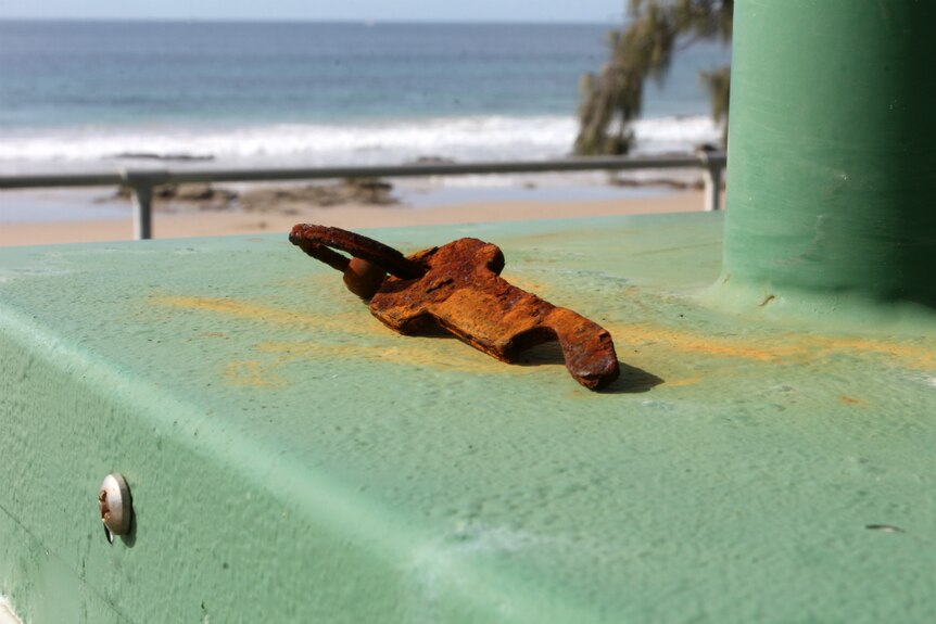 A rusty key lays on top of electrical box at the old Mooloolaba Esplanade Caravan Park with beach in background.