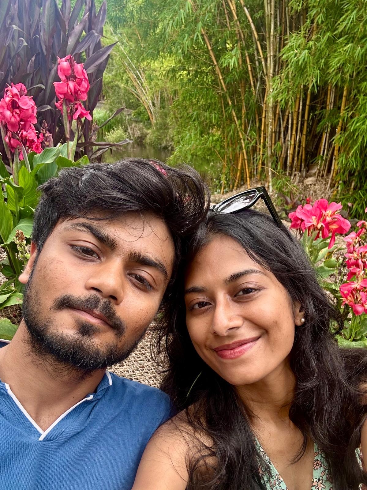 A young man and young woman in a garden smile at the camera