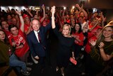 Bill Shorten and Susan Lamb, standing among supporters, hold up their hands in victory.