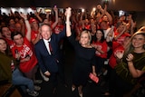 Bill Shorten and Susan Lamb, standing among supporters, hold up their hands in victory.