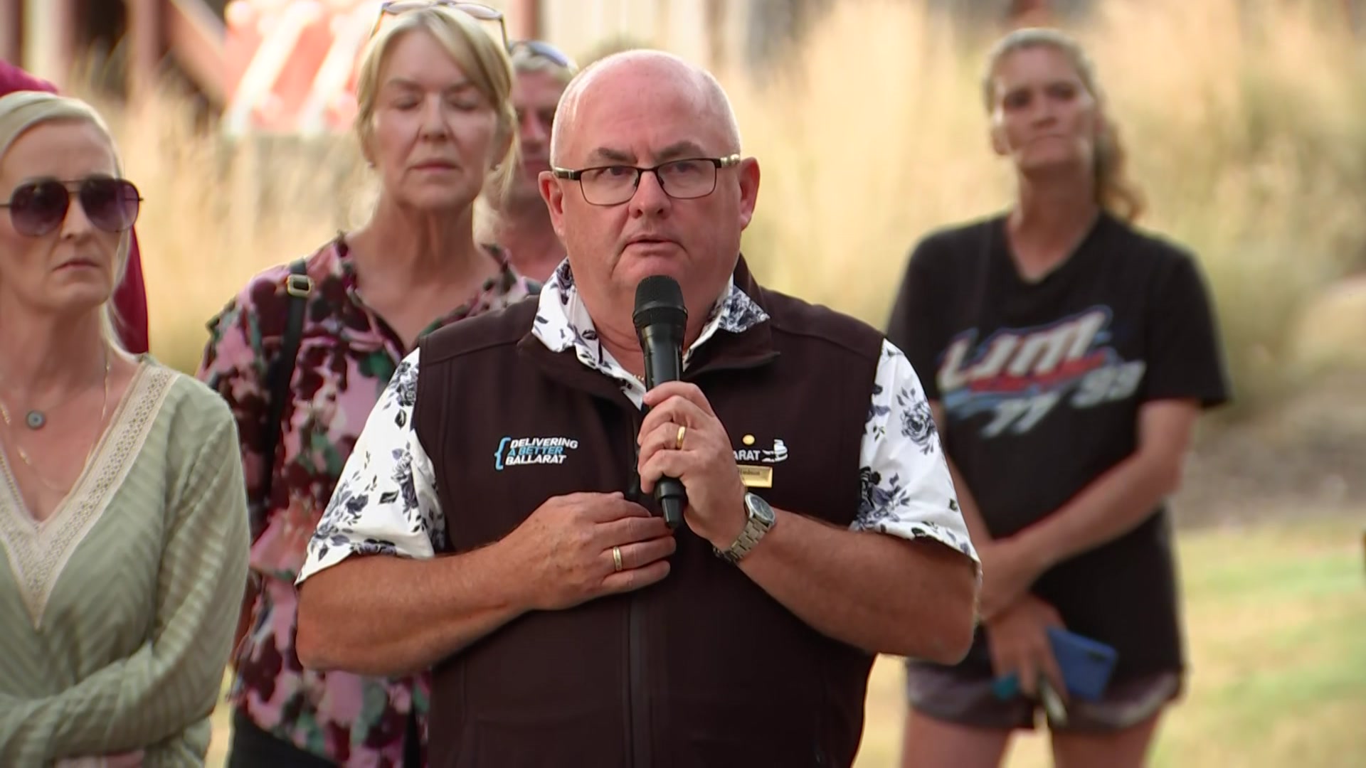 Des speaking into a microphone with others gathered around him.