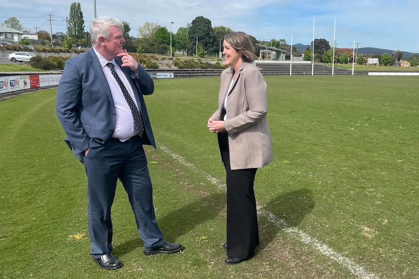 Two people standing on the sidelines of a sports field.