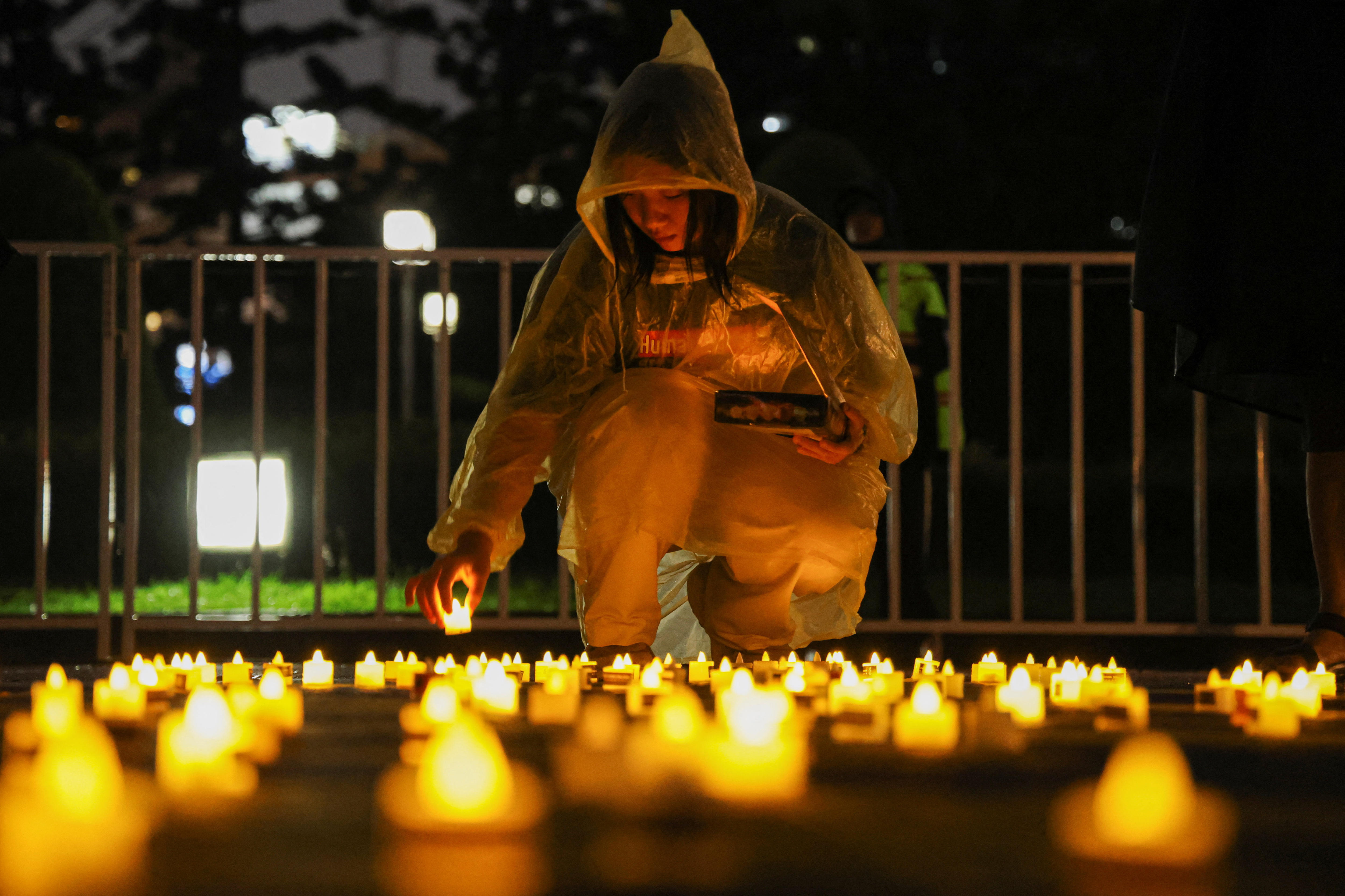 Una mujer coloca una vela en el suelo junto a otras velas.