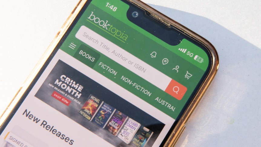 A phone screen displays Booktopia's green and white app with a search bar visible