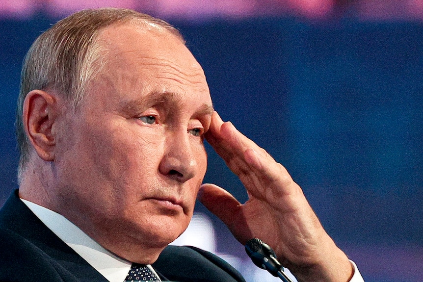 Russian President Vladimir Putin holds his fingers to his forehead.
