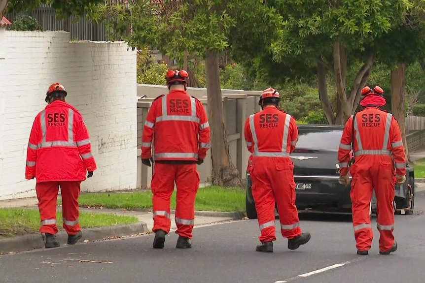 Four people in orange SES jackets, pants and helmets walk down a residential street in formation.
