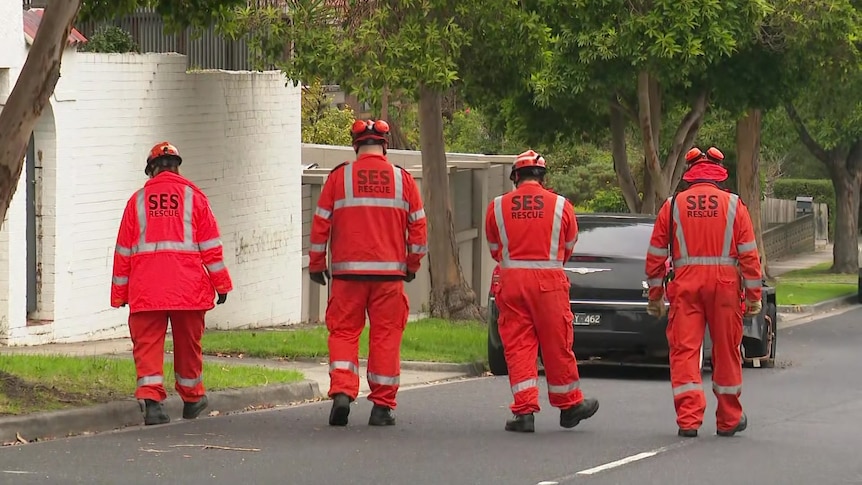 Four people in orange SES jackets, pants and helmets walk down a residential street in formation.