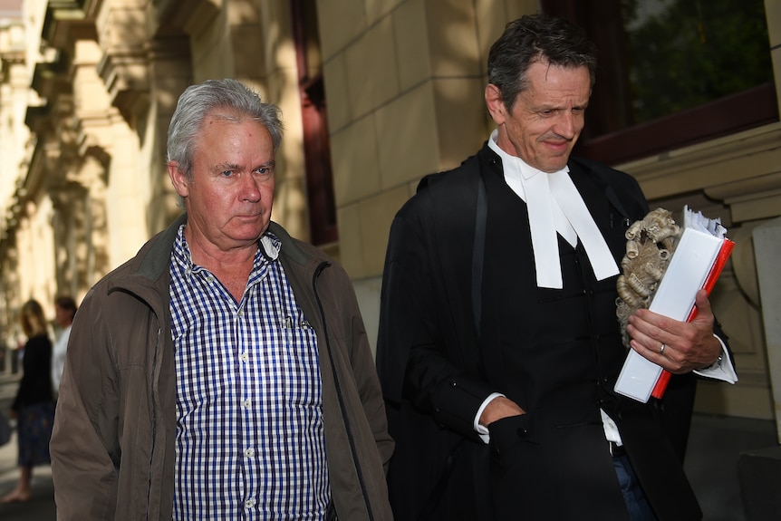 Peter Gant walking on a streete next to his lawyer who is wearing a legal robe