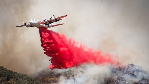 A C-130 waterbomber dropping retardant over a fireground