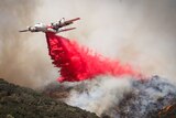 A C-130 waterbomber dropping retardant over a fireground