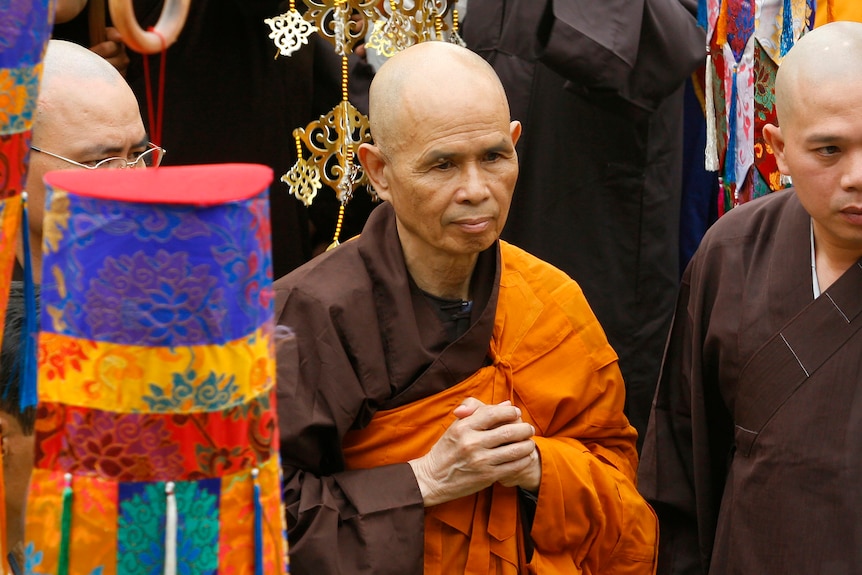 A monk in brown and saffron robes stands amongst others at a ceremony